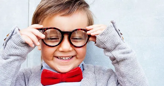 A smiling boy in round glasses and a red velvet bow tie
